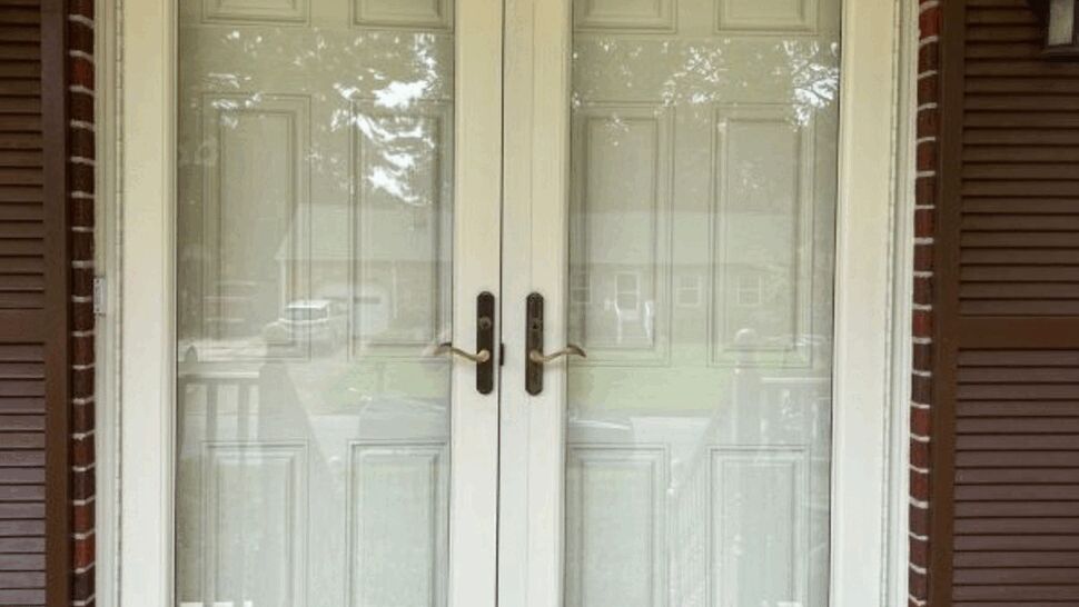 Close-up of white double glass storm doors with brass handles and brick trim