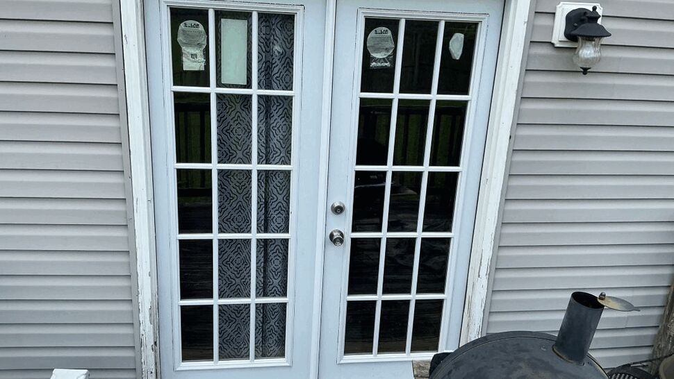Exterior white French doors with multiple grid panes set in vinyl siding