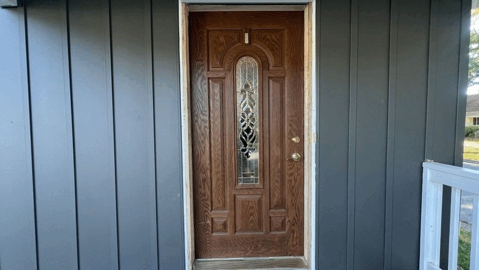 Wood single entry door with decorative privacy glass and brass hardware on a covered porch