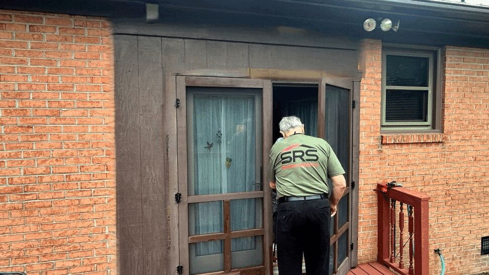 Technician opening wooden screen door on a red deck in front of a brick house