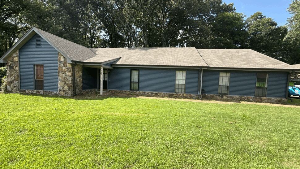 Front view of single-story blue sided ranch home with stone accents and lawn