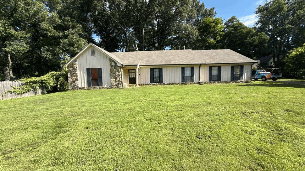 Wide front view of cream sided home with multiple windows and large lawn