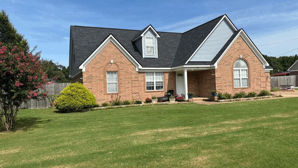 Bright front lawn and brick house with dark new roof under blue sky