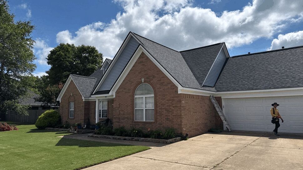 Front corner of brick home with roofer by the garage and ladder
