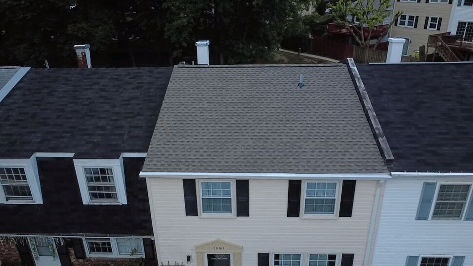 Aerial view of a gray shingle roof with white gutters on a townhouse
