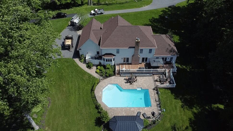 Aerial view of a multi-section shingle roof and backyard pool.
