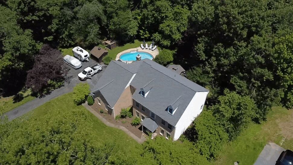 Aerial view of a large brick home with a gray shingle roof and backyard pool