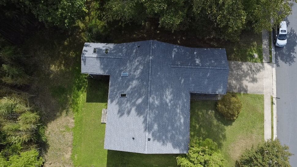 Aerial Residential Roof Overview | Wells Home Improvements Aerial view of a large gray shingle roof surrounded by trees and lawn.