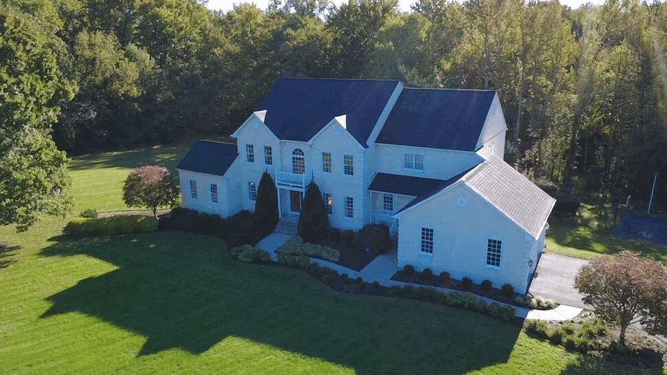 Aerial view of a large white home with dark roofing surrounded by trees.