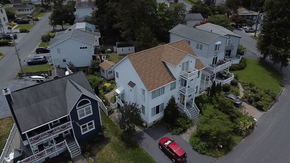 Angled aerial of a brown roof and neighboring homes on a residential street.