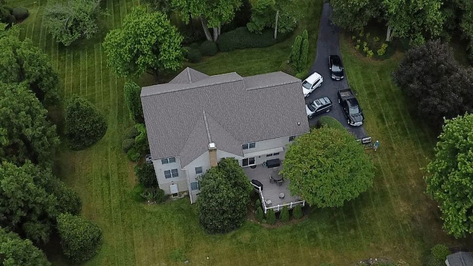 Drone image of rear deck and roof with patio furniture and surrounding lawn