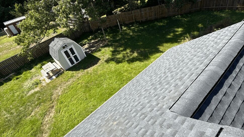Roof slope with new gray shingles overlooking a green backyard and shed.