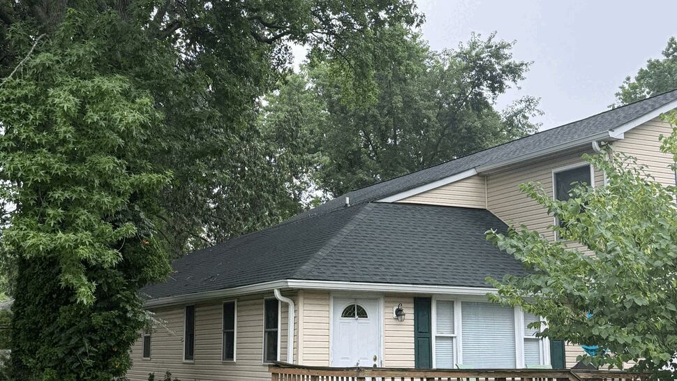 Full view of beige vinyl siding home with front porch and chain link fence