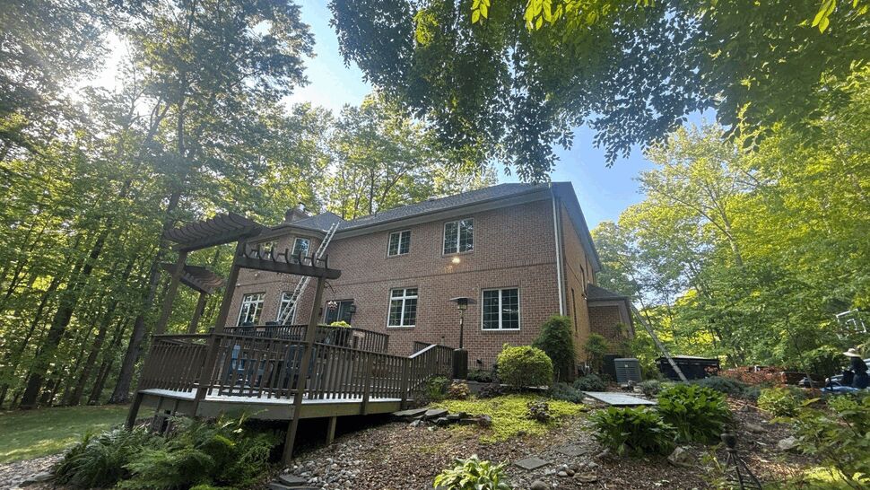 Brick Home Deck View | Wells Home Improvements Brick home with a raised wood deck surrounded by a wooded landscape.