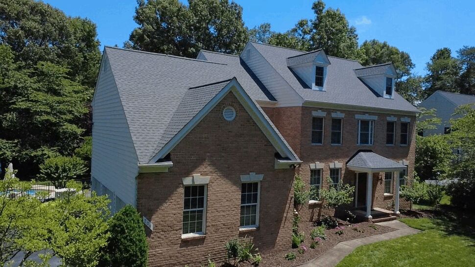 Front view of a brick home with gray shingles, dormer windows, and landscaped entry