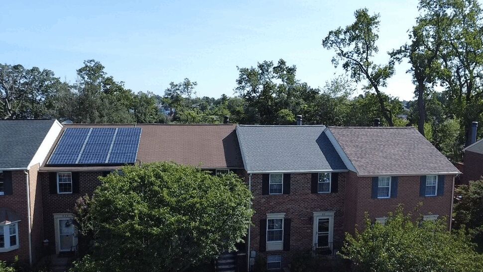 Brick Townhomes with Solar Roofs | Wells Home Improvements Brick townhomes with shingle roofs and solar panels surrounded by mature trees.