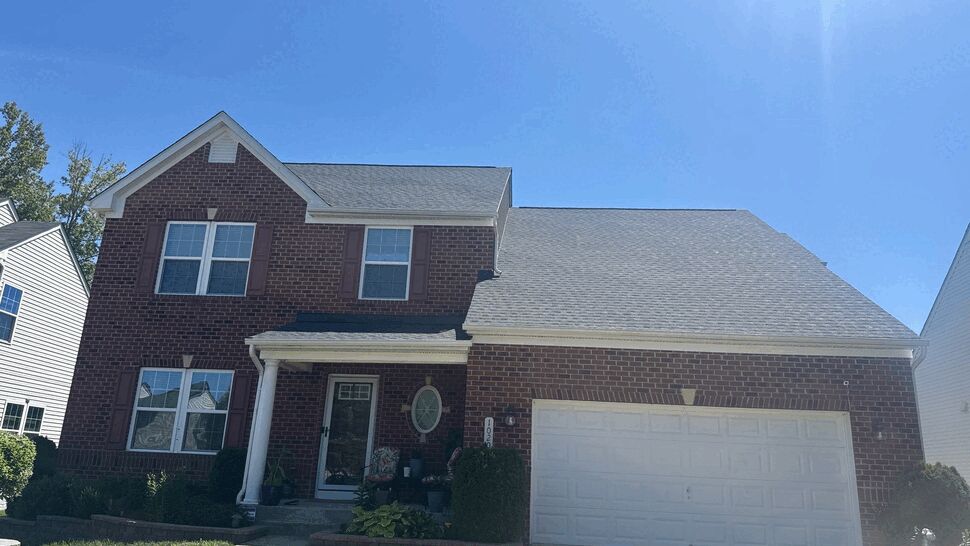 Two-story brick house with gray shingle roof, gutters, and attached garage