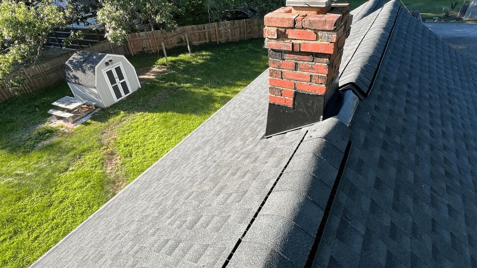 Brick chimney with new flashing on a gray shingle roof near a backyard.