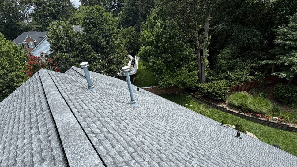 Close-up of gray shingle ridge vent | Wells Home Improvements Close-up of gray shingle ridge vent and roof vents overlooking backyard