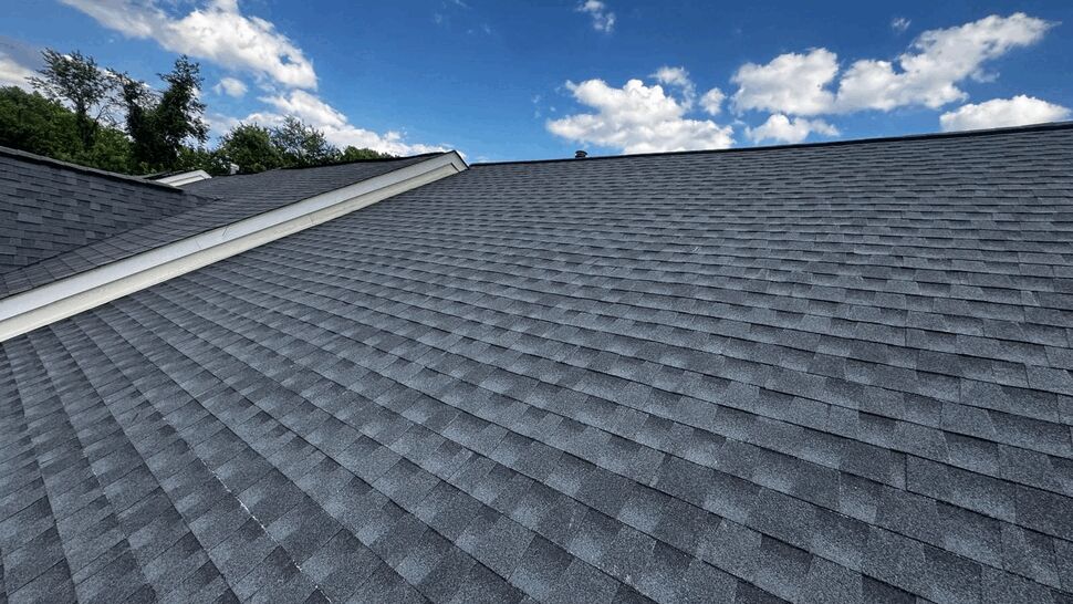 Close-up of uniform gray asphalt shingles across a residential roof under blue sky