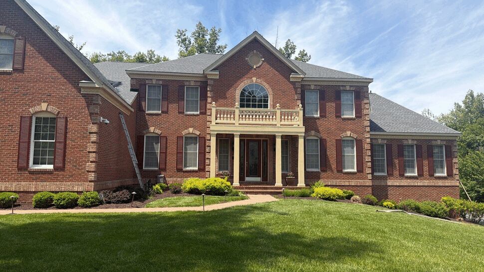 Two-story brick colonial with a newly installed gray shingle roof, ladder against the side and landscaped front lawn.