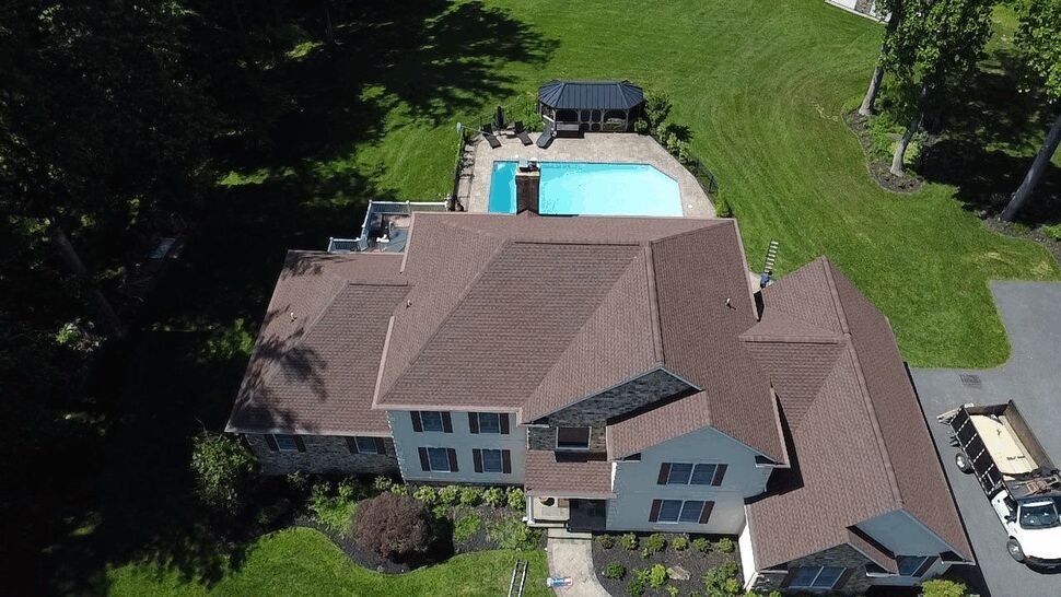 Aerial view of a complex shingle roof on a landscaped home.