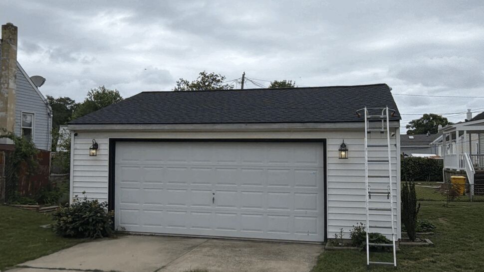 Detached two-car garage with fresh dark shingle roof and ladder on the side