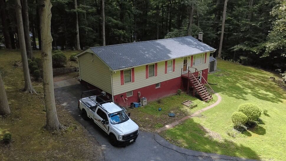 Aerial view of a raised ranch home with new shingle roof and a Wells Home Improvements truck in driveway