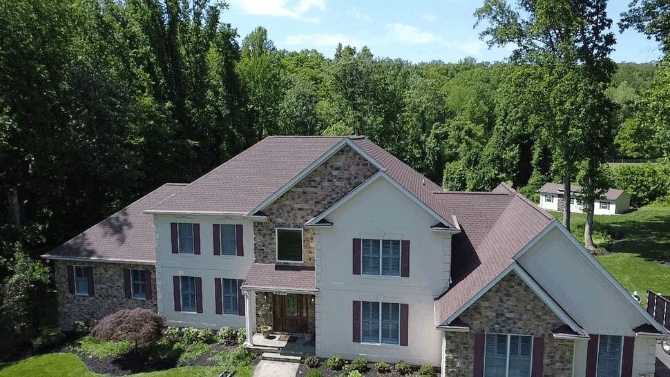 Front aerial view of a shingle-roofed home surrounded by trees.