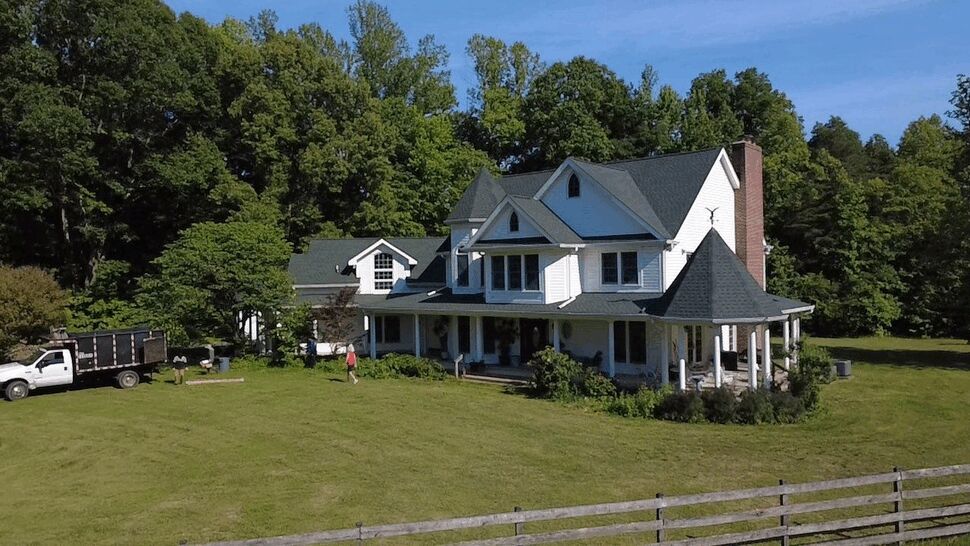 Front view of a farmhouse with a wraparound porch, white siding, and dark shingle roof.