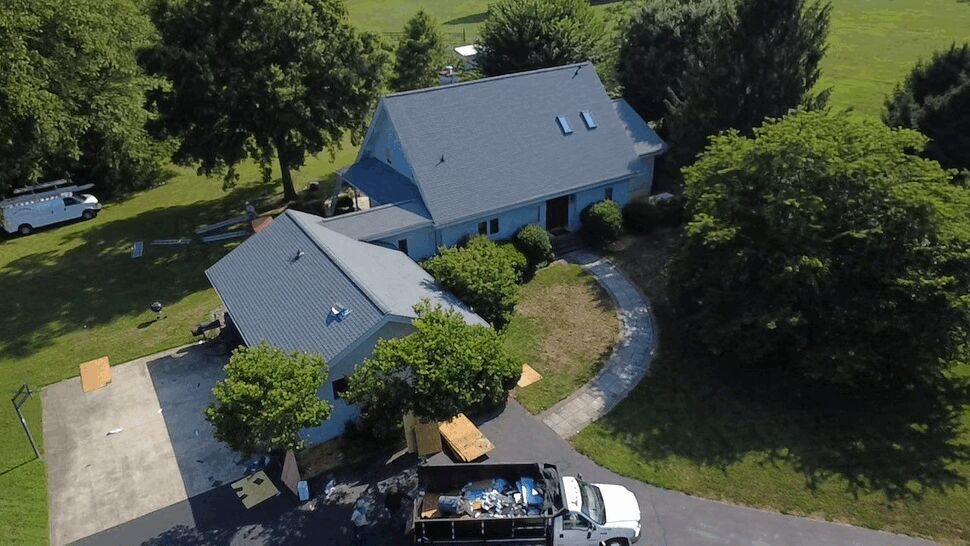 Roof Installation at Driveway | Wells Home Improvements Front-angle view of home with roofing truck and debris container in driveway.