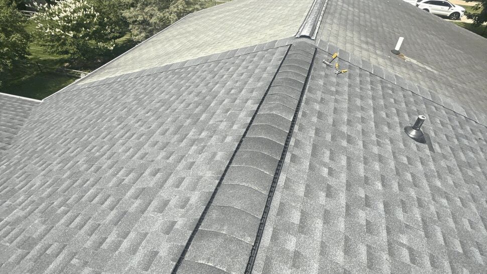 Bird's-eye view of a gray shingle roof ridge with ridge vent and yard beyond