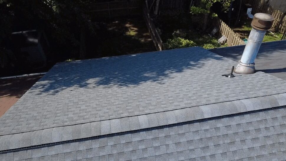 Close-up Gray Shingle Roof with Vent | Wells Home Improvements Close-up aerial view of a gray shingled roof with a vent pipe.