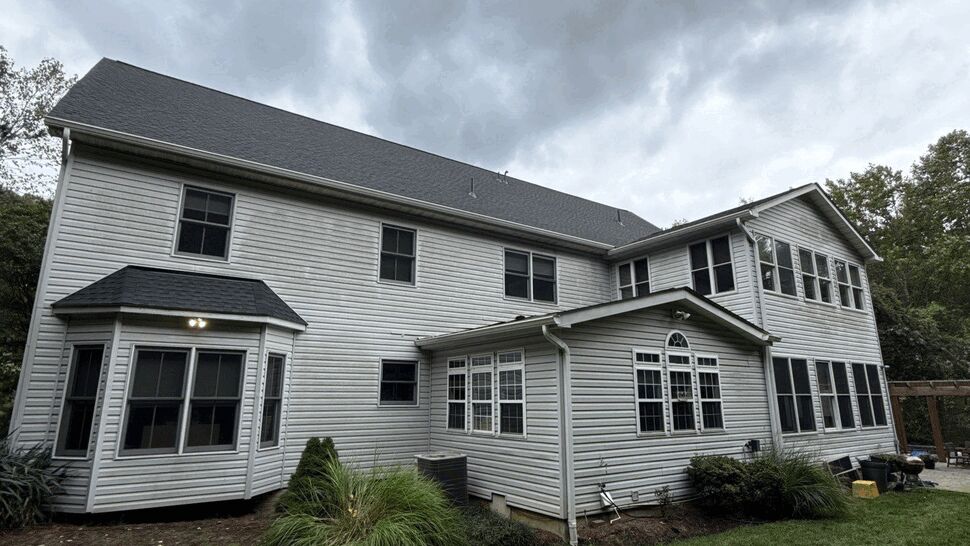 Large gray-sided home with dark roof, multiple windows, and landscaped lawn.