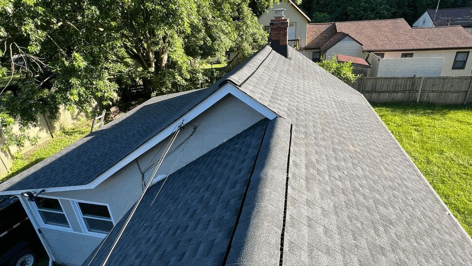 Aerial view of a gray shingled roof ridge with vented cap and surrounding trees.