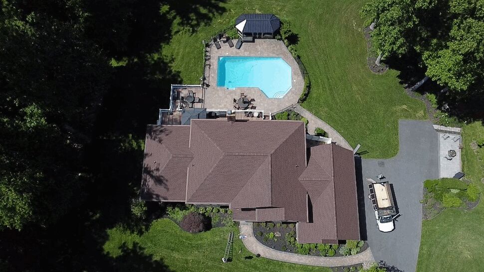 Overhead view of a large shingle roof beside a backyard pool.