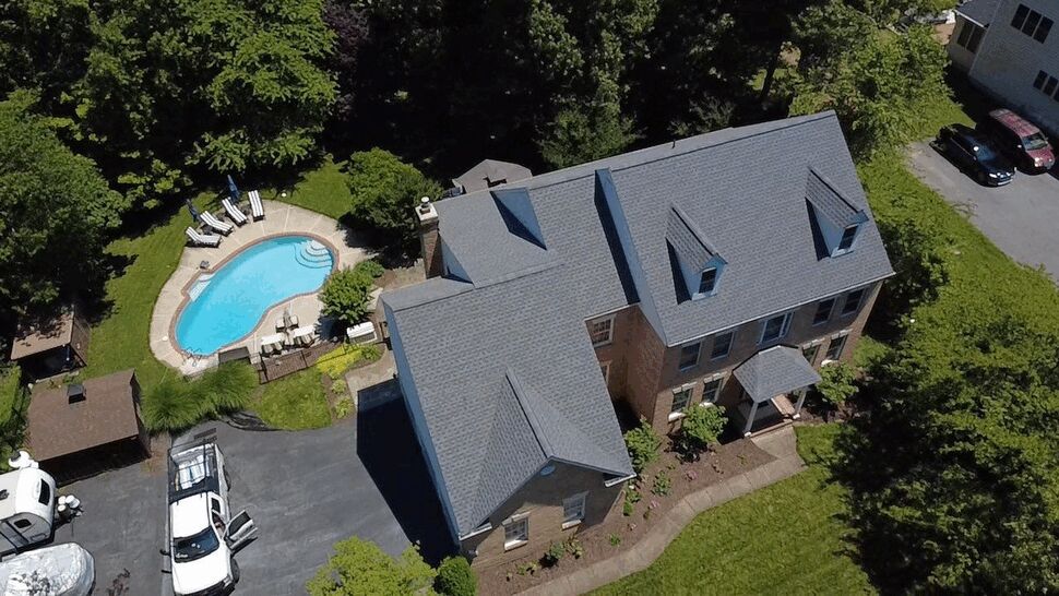 Overhead view of a brick home with gray roofing, dormers, and a swimming pool