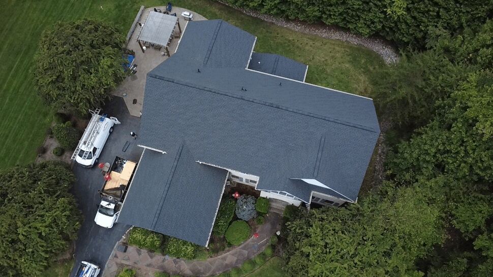 Overhead Shingle Roofing View | Wells Home Improvements Overhead view of a large dark shingle roof with workers and vehicles nearby.