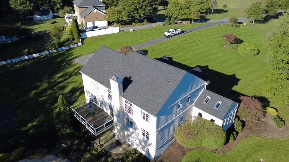 Rear Home Roofing and Deck | Wells Home Improvements Aerial rear view of a white home with gray roofing and a rear deck.
