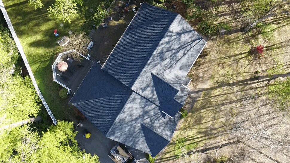 Overhead view of a home's roof and backyard deck with surrounding trees and shadows.