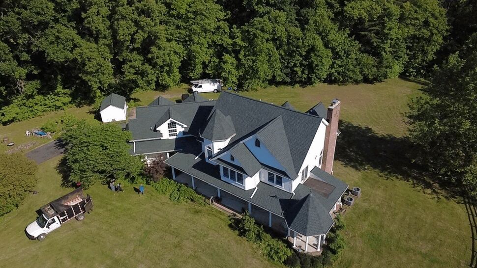 Roof Project Site Overview | Wells Home Improvements Oblique overhead view of a house with new shingles, crew truck, and tree line in the background.