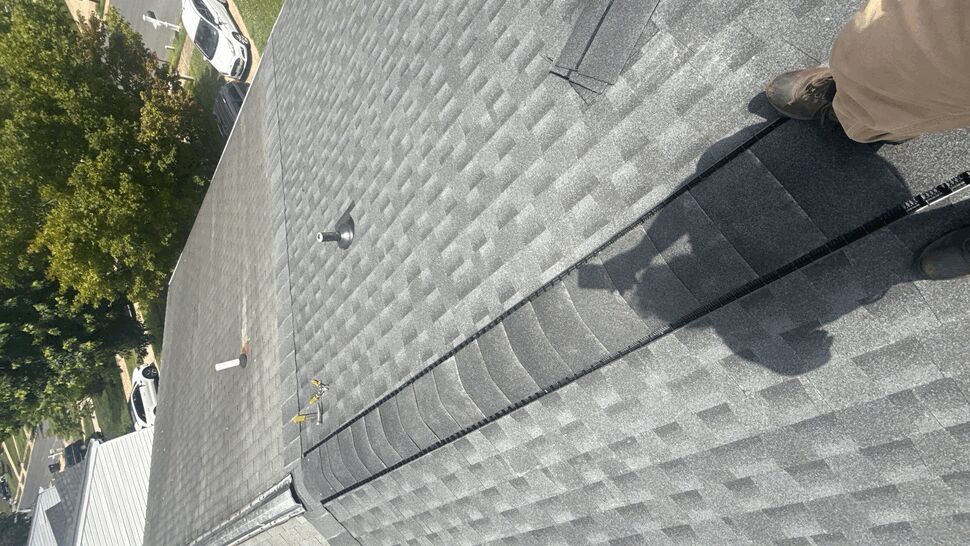 Close-up of ridge vent installation on gray shingles with worker shadow and tools