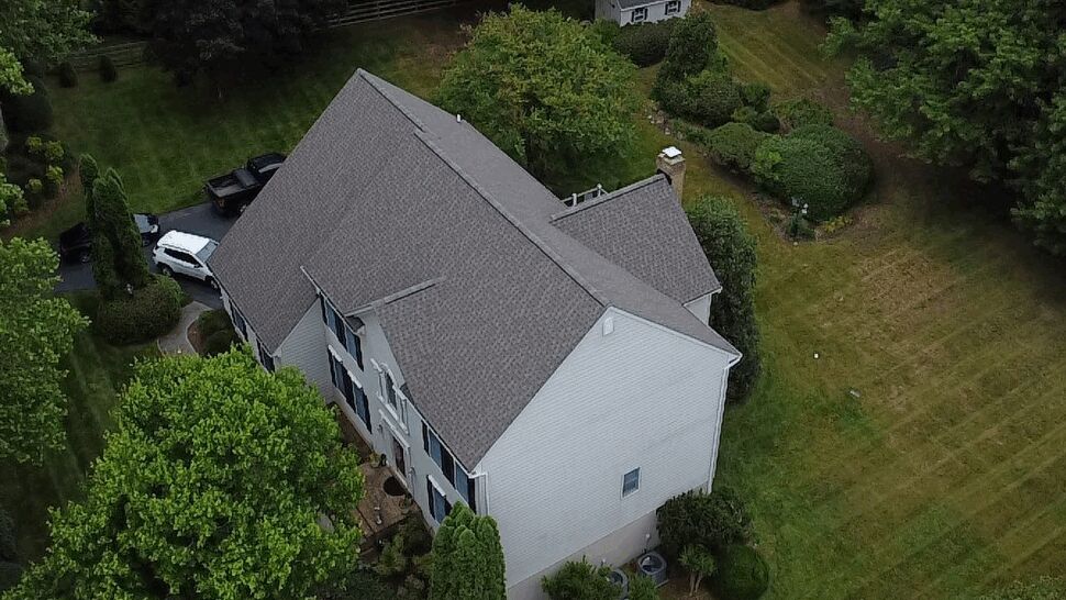 Oblique drone angle of residential roof and siding with surrounding trees
