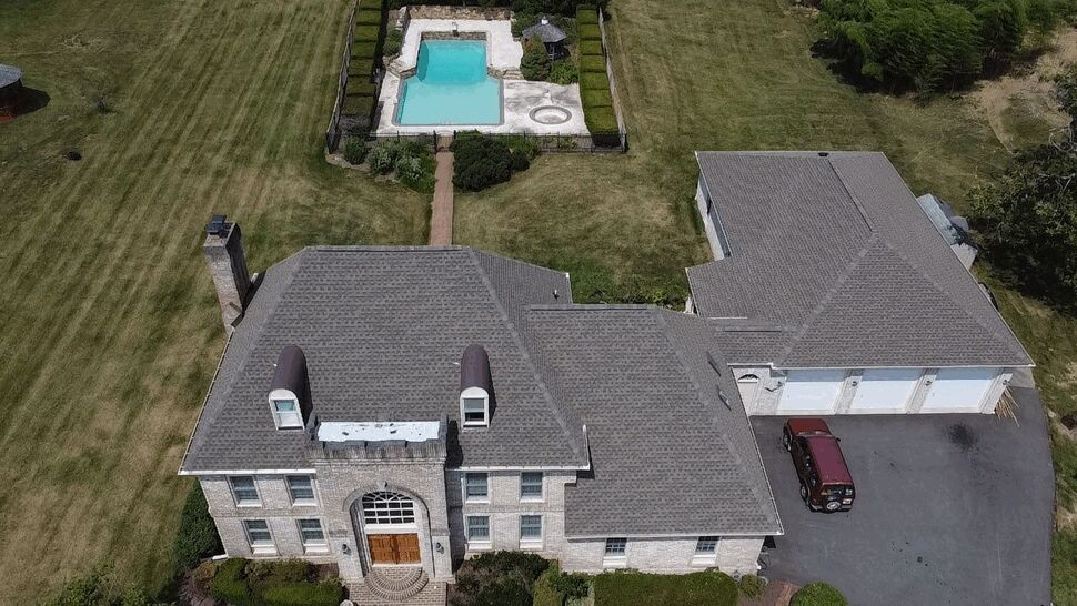 Front aerial view of home facade with windows, roof, and pool beyond