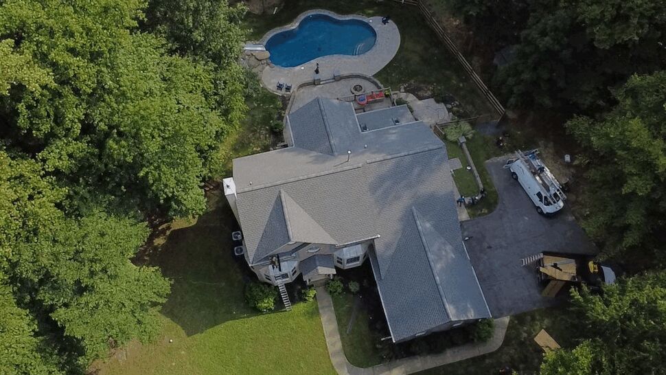 Suburban Home Roofing Project | Wells Home Improvements Top-down view of a large suburban home's roof with work trucks and a pool.