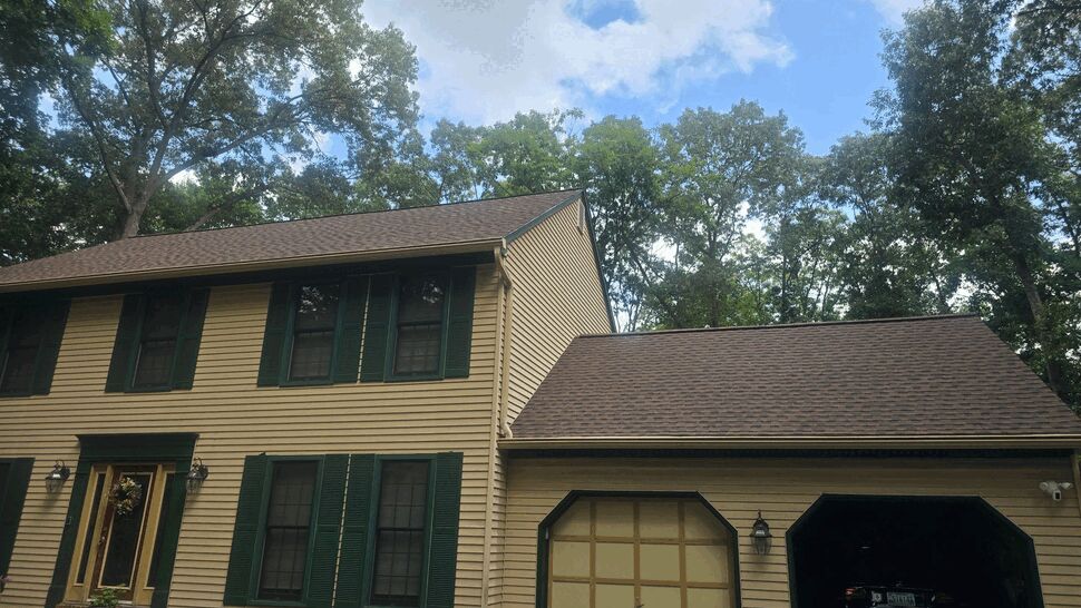 Tan suburban home with dark shutters, attached garage, and shingle roof