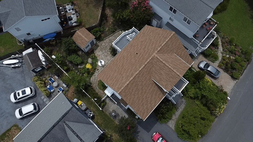 Aerial top-down view of a brown shingle roof on a suburban home.