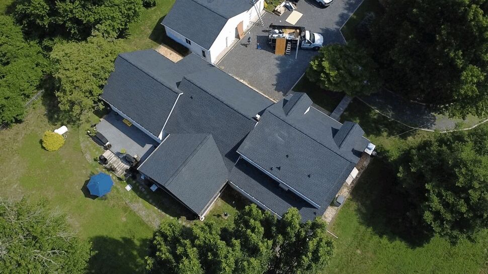 Top-Down Roofing Inspection | Wells Home Improvements Top-down drone image of interconnected dark shingle roof sections and lawn