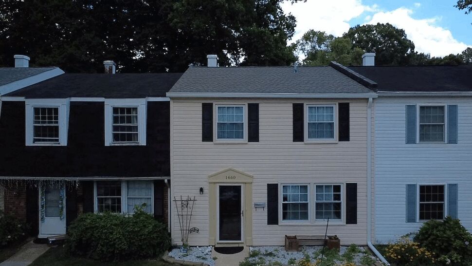 Front elevation of a townhouse with beige siding, black shutters, and gutters