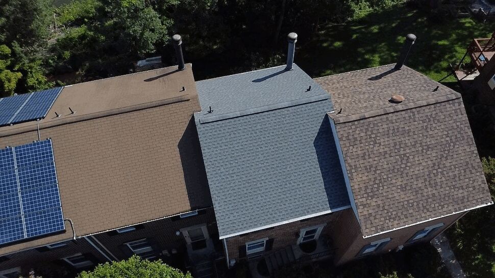 Townhouse Roof Shingle Detail | Wells Home Improvements Close aerial view of townhouse roofs with brown and gray shingles and solar panels.